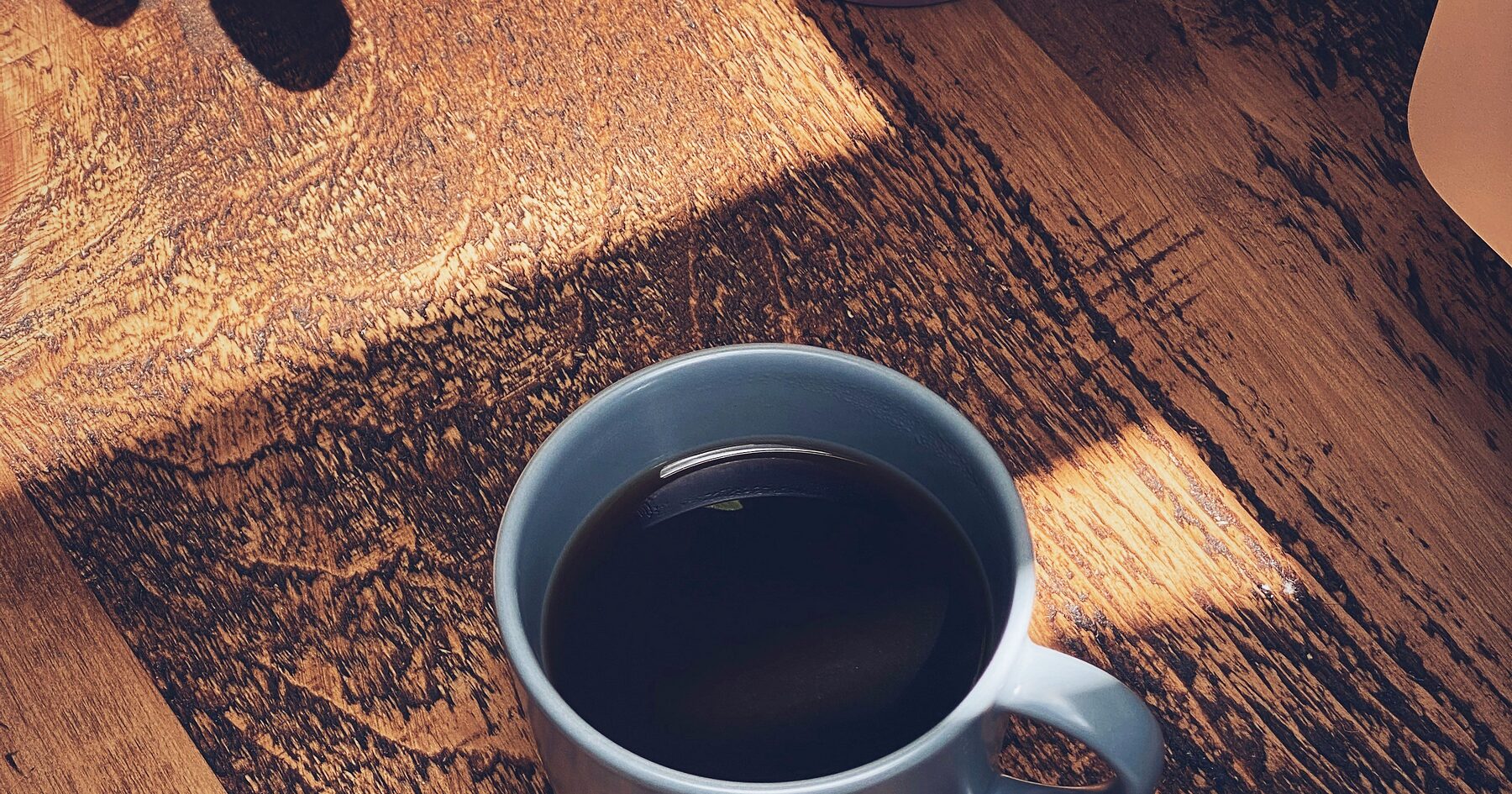 A cup of black coffee on a wooden table in low afternoon light