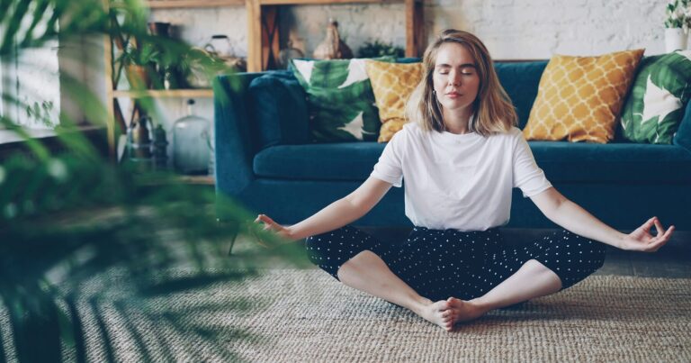 A person sitting cross-legged on a rug with their eyes closed