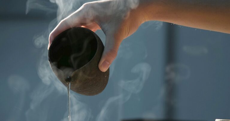 A hand pouring tea from a clay pot, steam rising in dim light