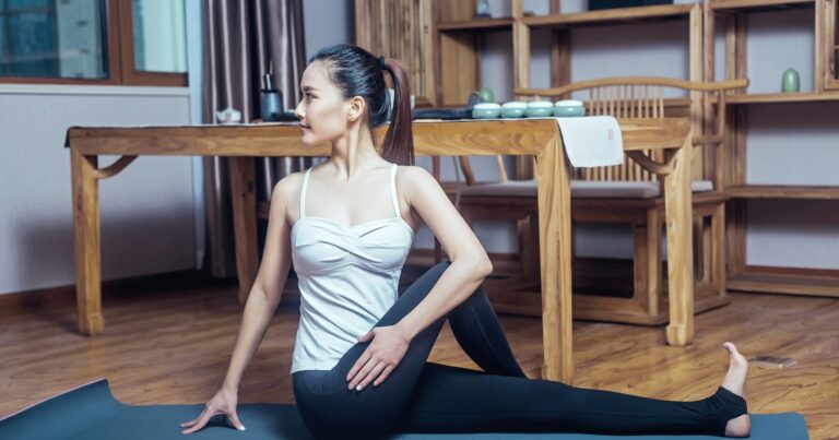 A person doing a seated stretch on a mat in a warm wooden room