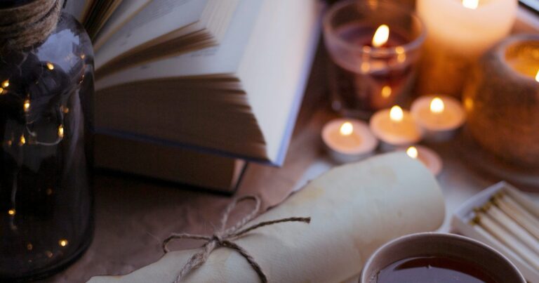 An open book beside lit candles on a table in the evening
