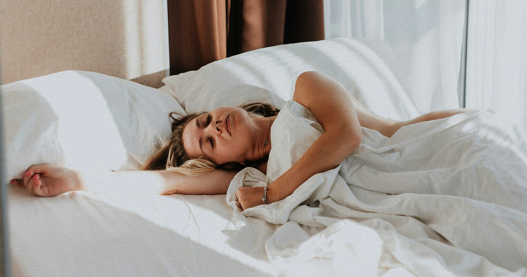 A person waking and stretching in a bed with white linen