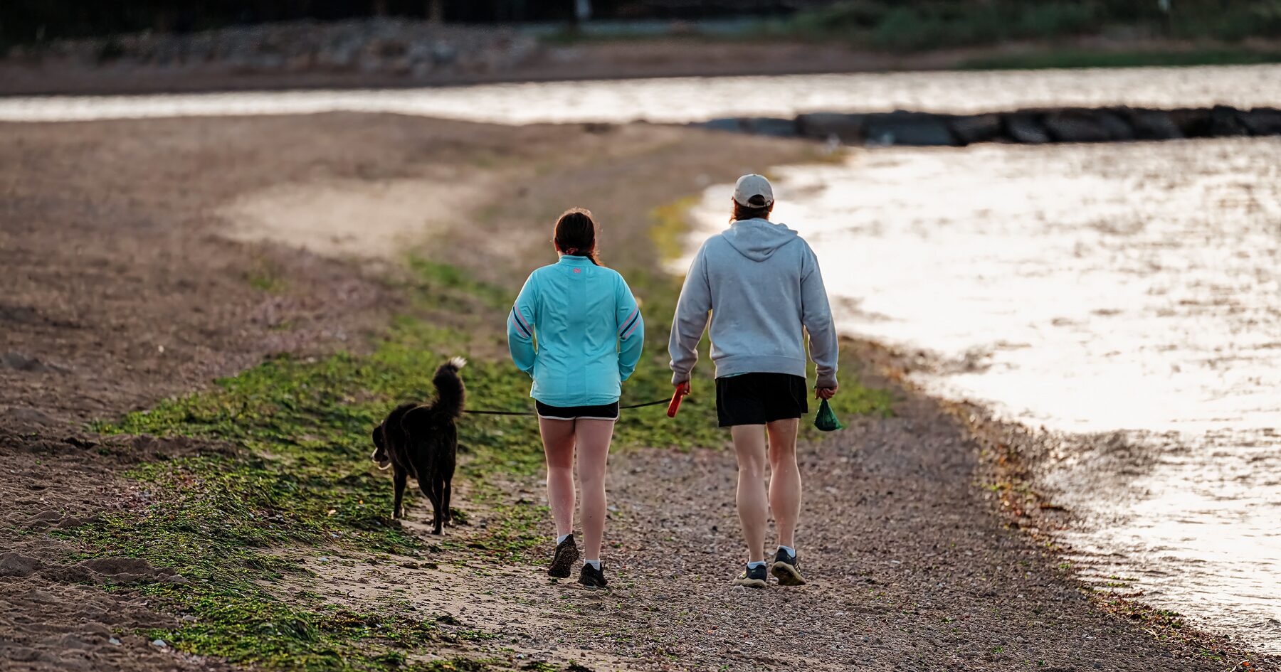 Two people walking a dog along a gravel trail