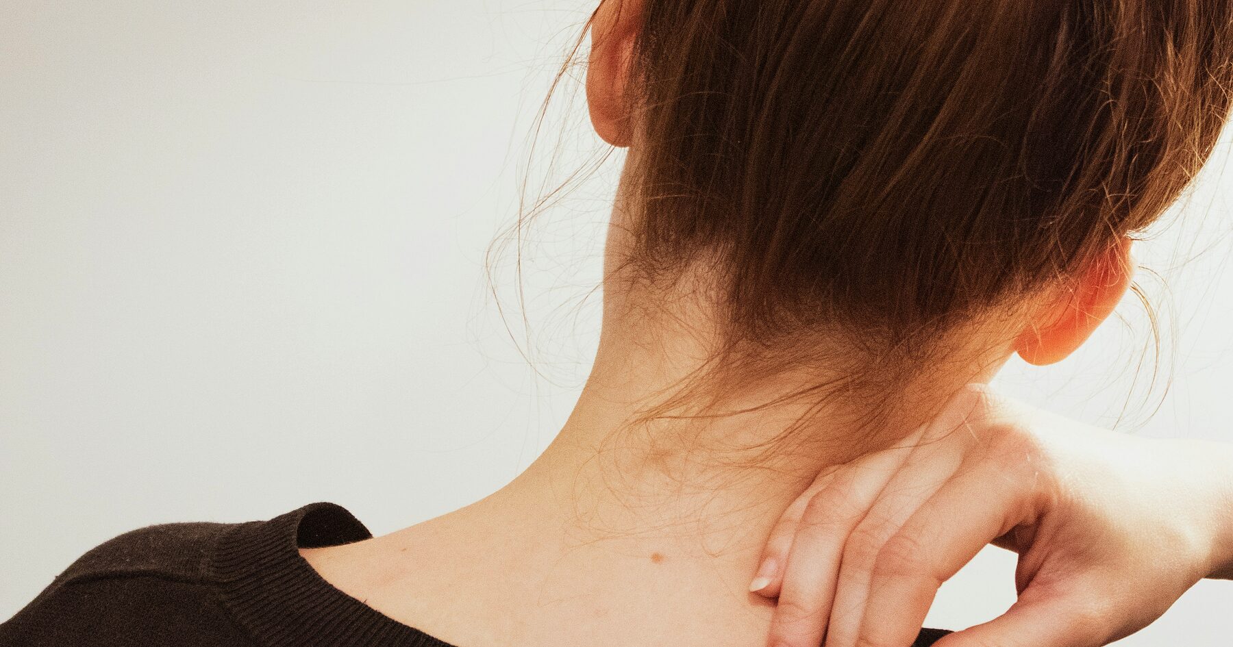 A person reaching back to rub the base of their neck
