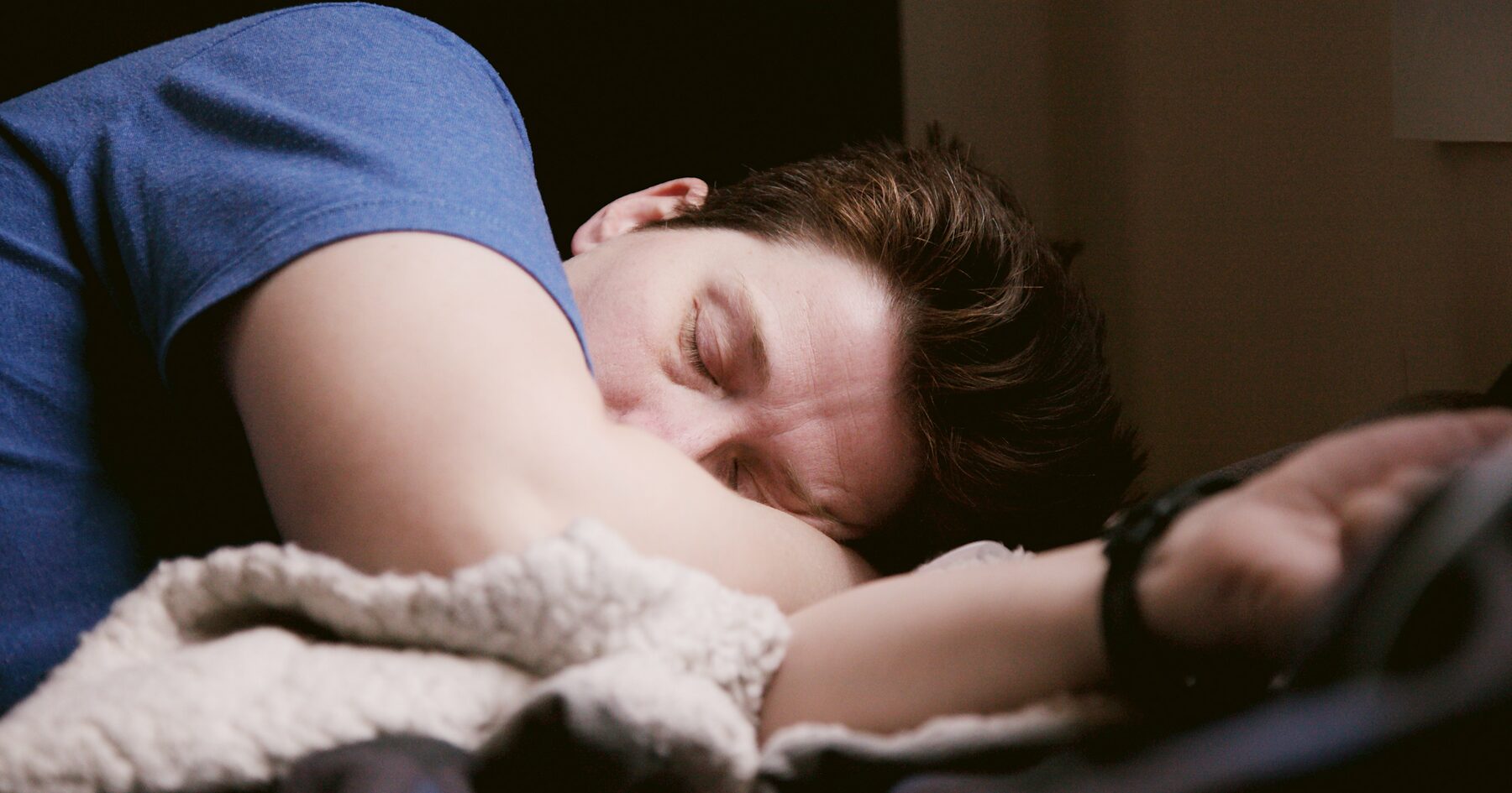 A person asleep with one arm resting over a blanket