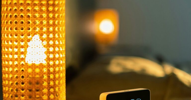 A warm bedside lamp lit beside a digital clock in a dim bedroom
