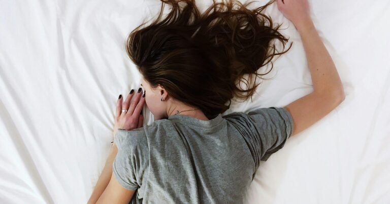 A woman lying face down in white bedding, awake in the small hours