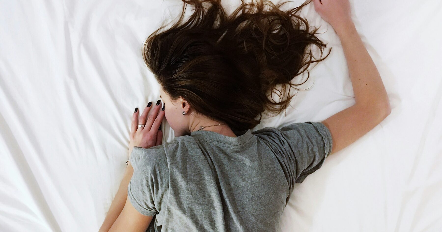 A woman lying face down in white bedding, awake in the small hours